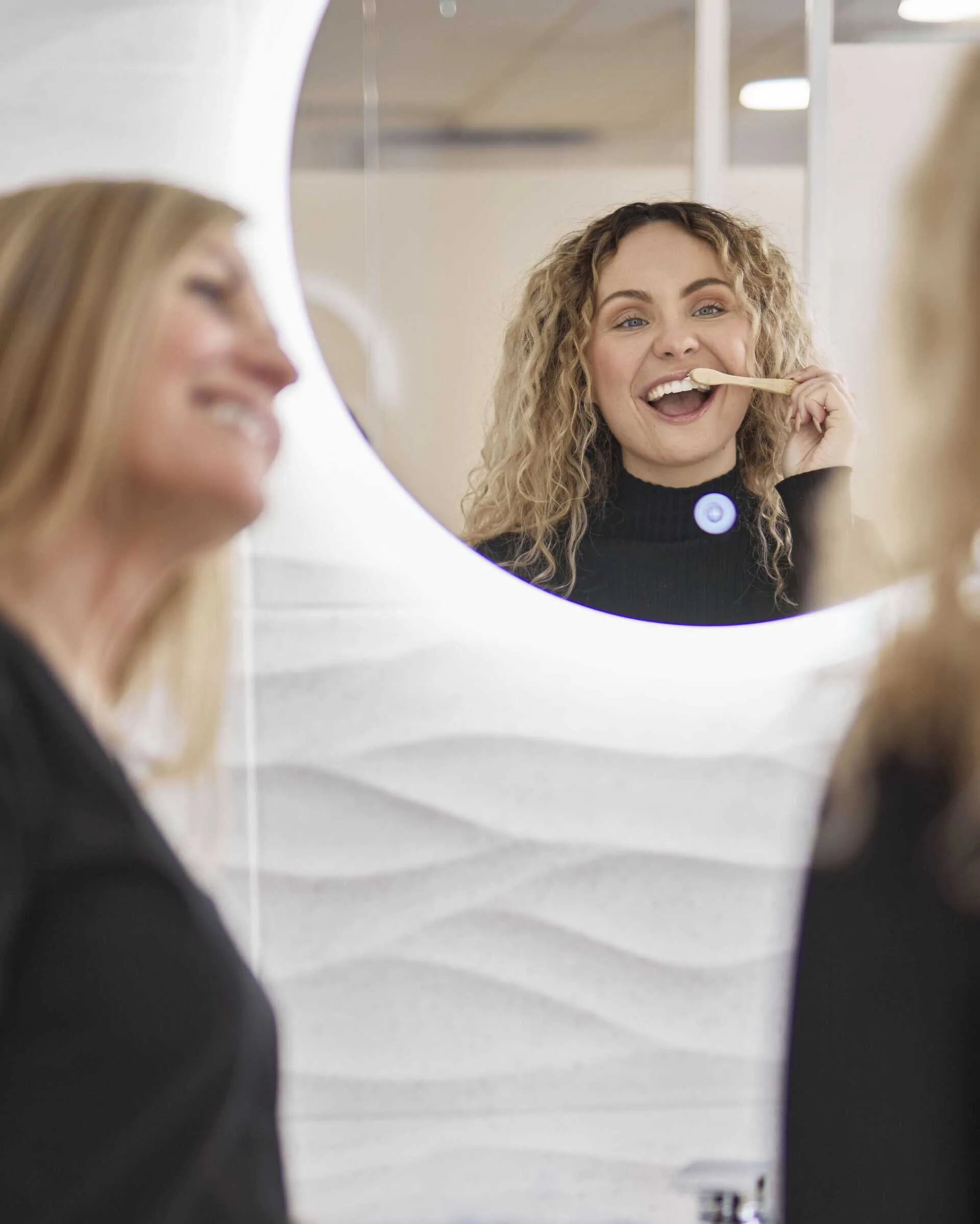 Lady brushing teeth in mirror beyond dental