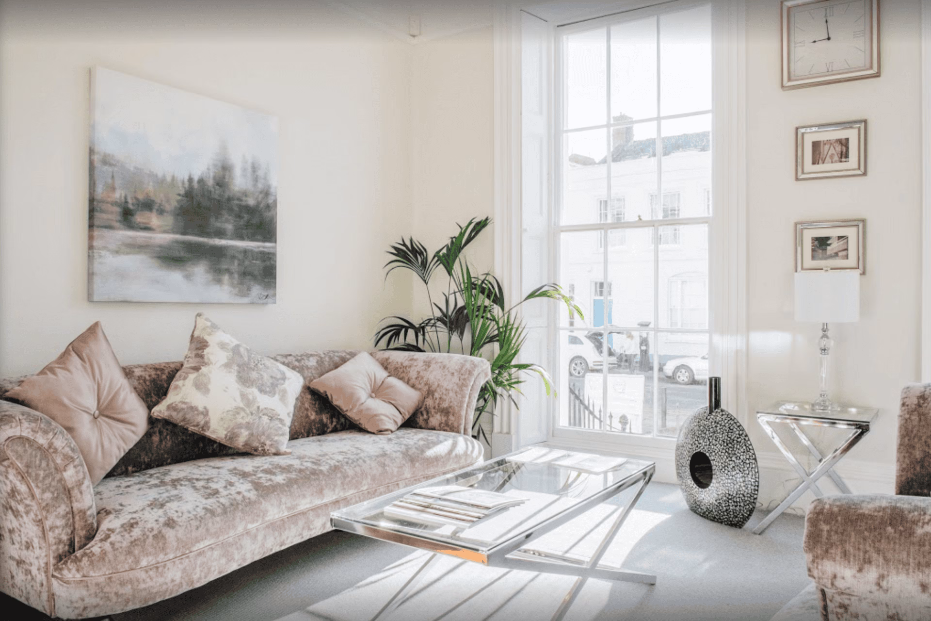 Reception area at Beyond Dental Cheltenham with a velvet sofa, glass coffee table, armchair, large sash window and soft neutral décor.