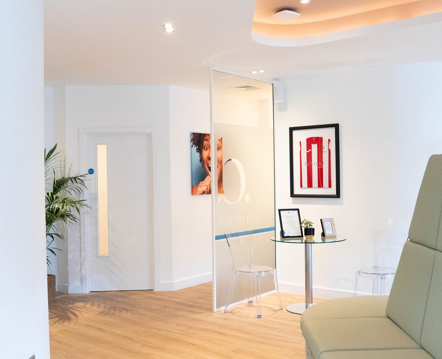 Clean dental clinic waiting lounge with glass partitions and framed jersey.