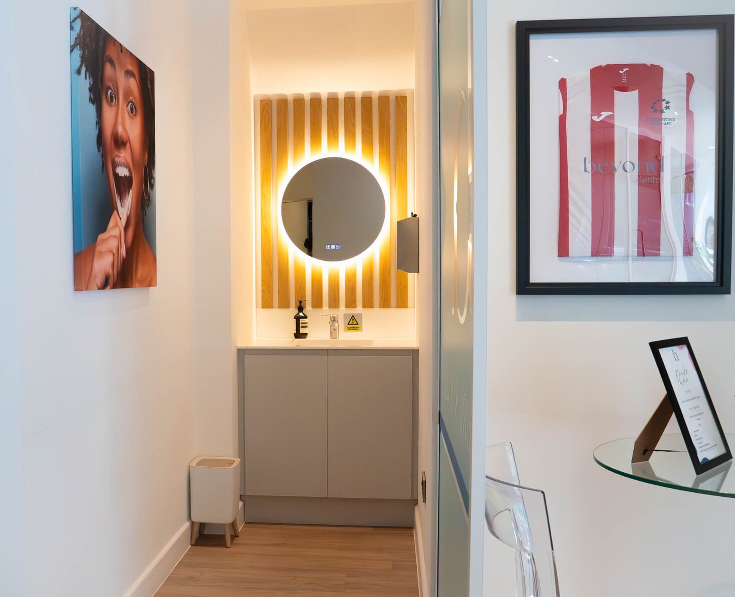 Dental clinic vanity area with backlit round mirror and framed football jersey.