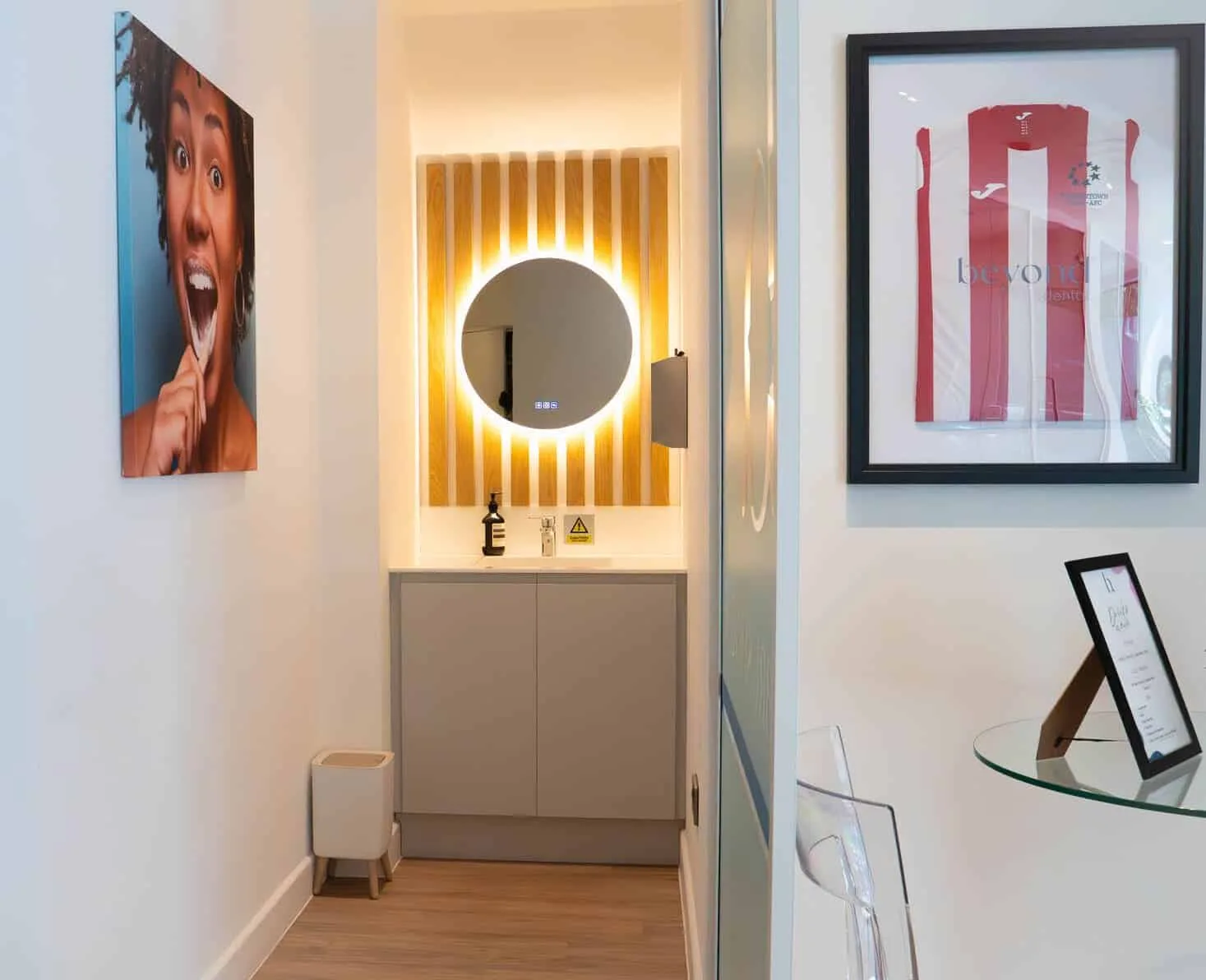 Dental clinic vanity area with backlit round mirror and framed football jersey.