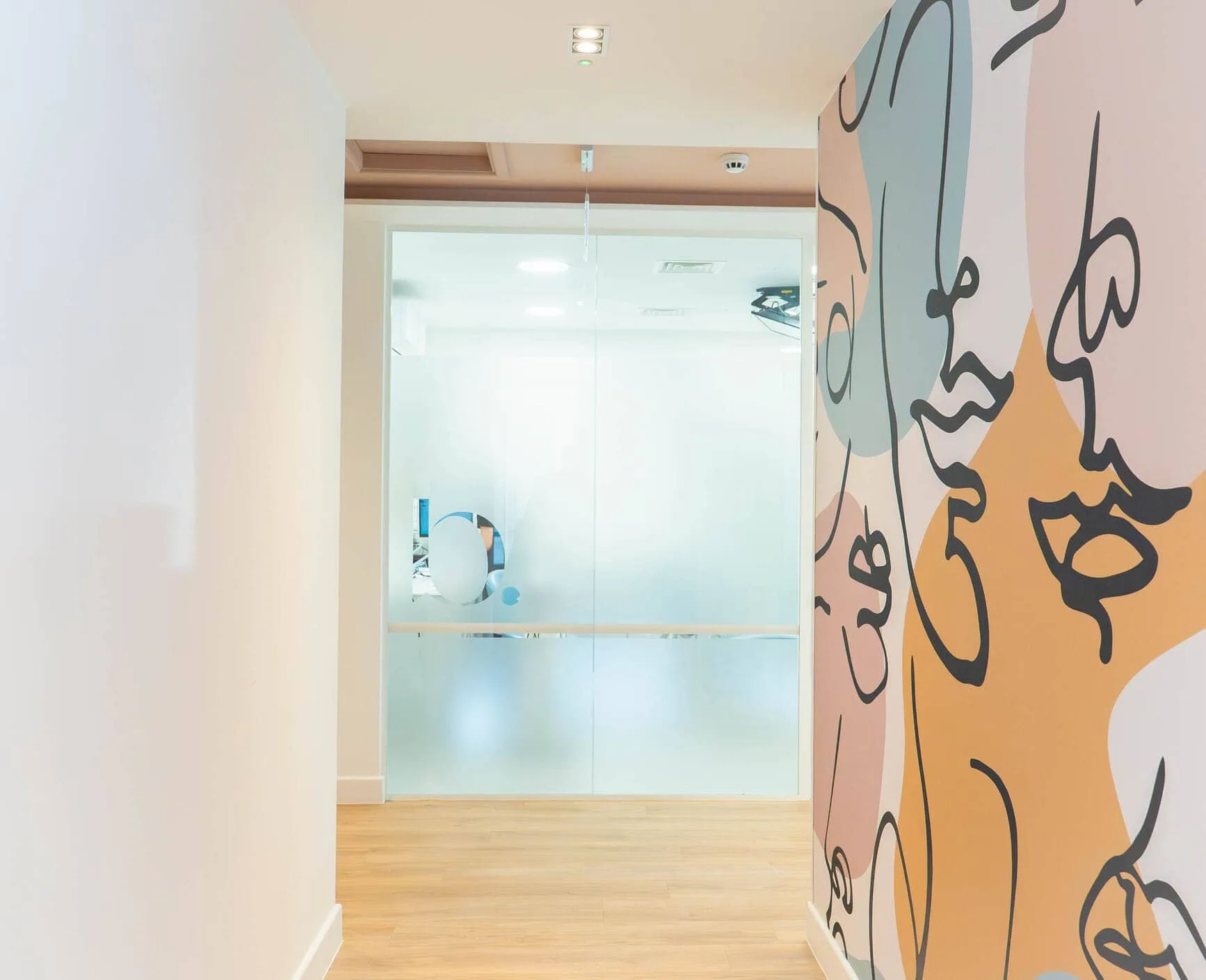 Dental clinic corridor with abstract face mural and frosted glass door.